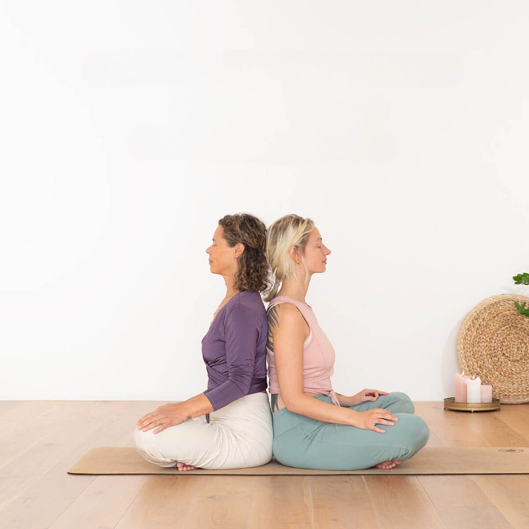 yoga pose 2 women back's against each other